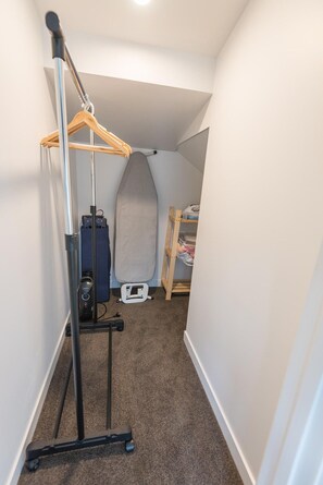 A narrow hallway with a vacuum cleaner, ironing board, and a wooden rack. - Lakeside Gem - Lake Views, Kayaks, Sleeps 8 (Rotorua)