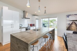 A modern kitchen with white cabinets, a large island with stools, and pendant lighting.