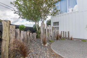 A building with a white exterior, a gravel driveway, and a wooden fence. - Lakeside Gem - Lake Views, Kayaks, Sleeps 8 (Rotorua)