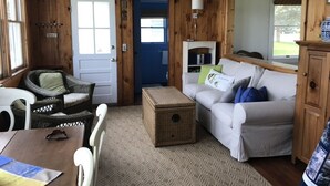 A cozy room with a white sofa, wicker chairs, a small table, and a fireplace. - Ocean Front Cottage! (Westport)