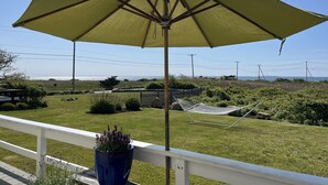 A yellow umbrella on a white railing overlooking a grassy area with a hammock and a potted plant. - Ocean Front Cottage! (Westport)