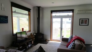 En stue med sofa, fjernsyn, pejs og en skydedør, der fører ud til en balkon.
