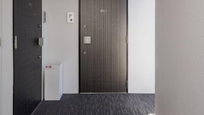 Een moderne hal met een donkerhouten deur waarop het cijfer 903 staat, een klein wit paneel met een keypad, en een vloerbedekking.