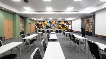 Uma sala de conferências com mesas, cadeiras, um projetor e um painel decorado com arranjos florais circulares.