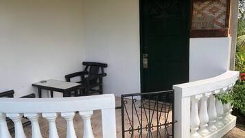 A covered outdoor seating area with a green door, a white railing, and a tiled floor.