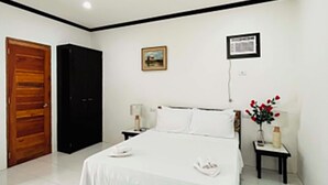 A bedroom with a bed, a wooden door, a black wardrobe, a small table with a lamp, and a picture on the wall. - Jupiter's Garden Resort (Lawaan)