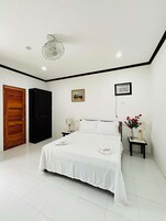 Un dormitorio con cama, puerta de madera, armario negro, mesita de noche con lámpara y un cuadro en la pared.