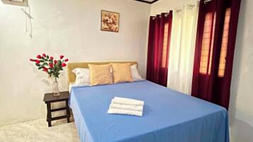 A bedroom with a bed, a bedside table with a vase of flowers, a ceiling fan, and curtains.