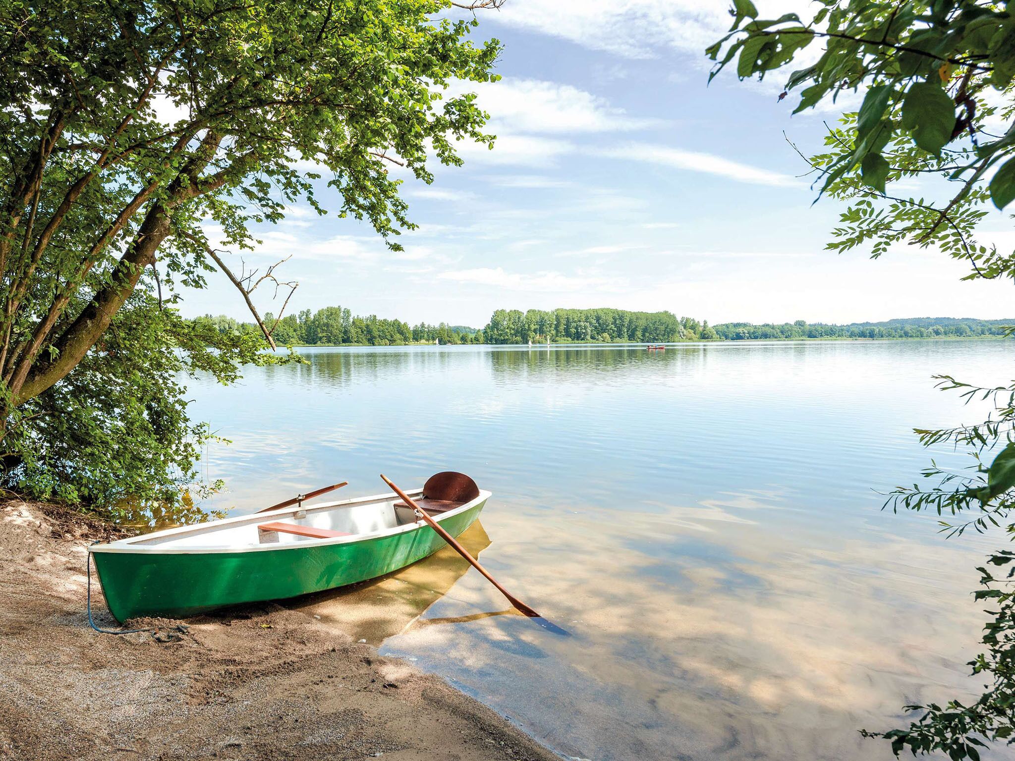Ein ruhiger See mit einem grünen Boot, das am Ufer festgemacht ist, umgeben von Bäumen.