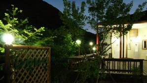 A garden with a wooden fence, a wooden deck, and a building with a light on the porch.