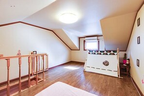 A room with a sloped ceiling, wooden flooring, a wooden railing, a window, and a small table.