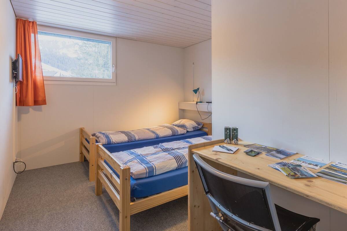 Acomodação compacta, com um quarto, cama, escrivaninha e cadeira.