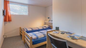Acomodação compacta, com um quarto, cama, escrivaninha e cadeira.