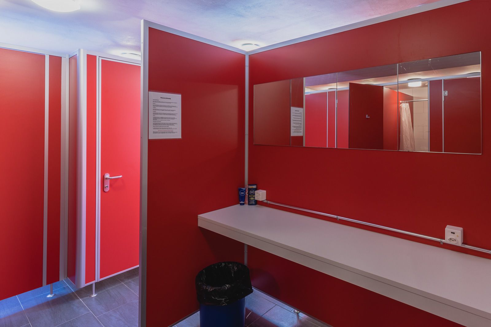 A red restroom with a white sink, a mirror, and a trash bin.