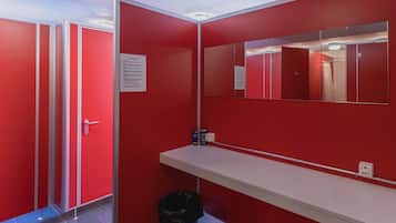 A red restroom with a white sink, a mirror, and a trash bin.