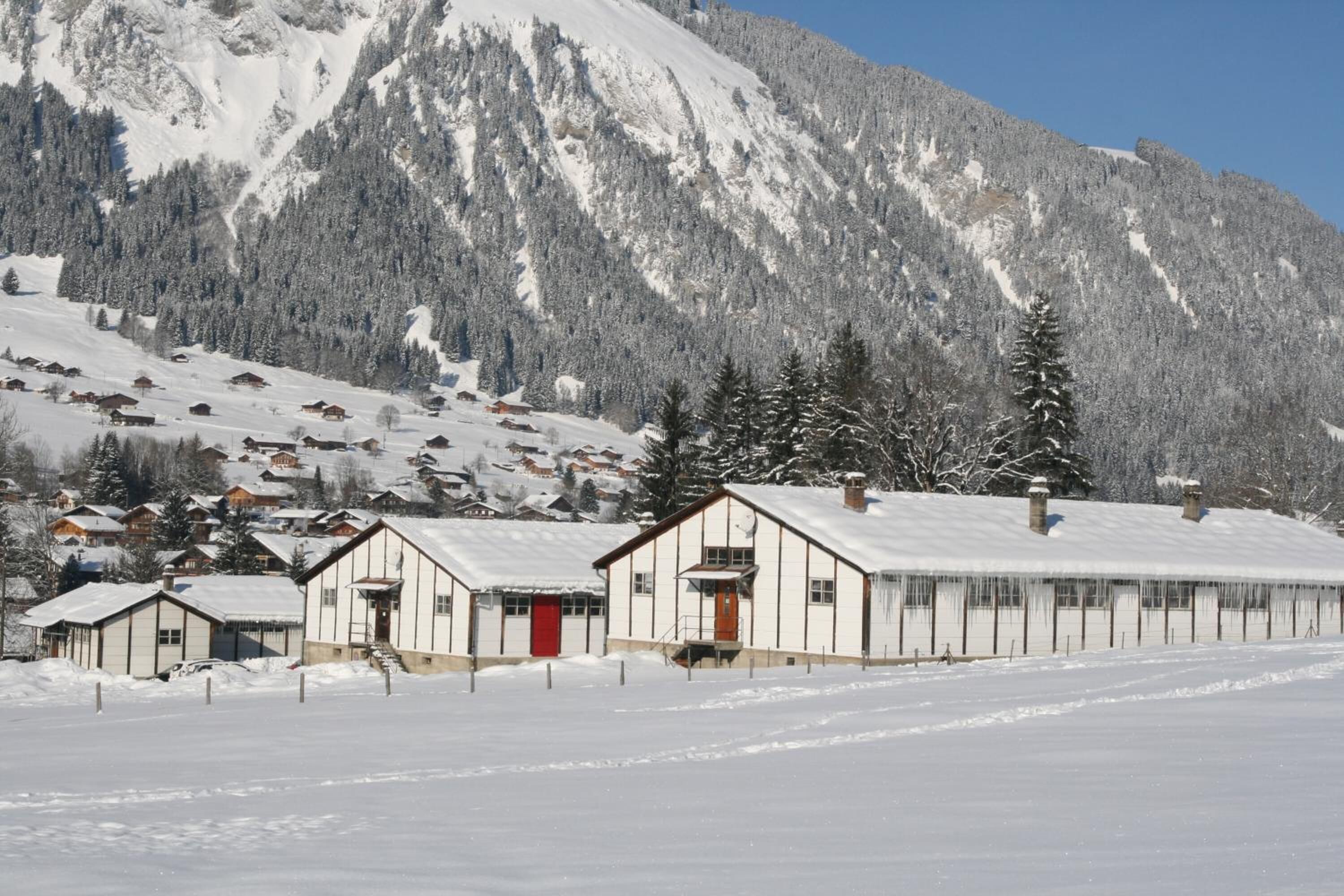A snow-covered mountain with a row of wooden cabins and a large building with a red door.