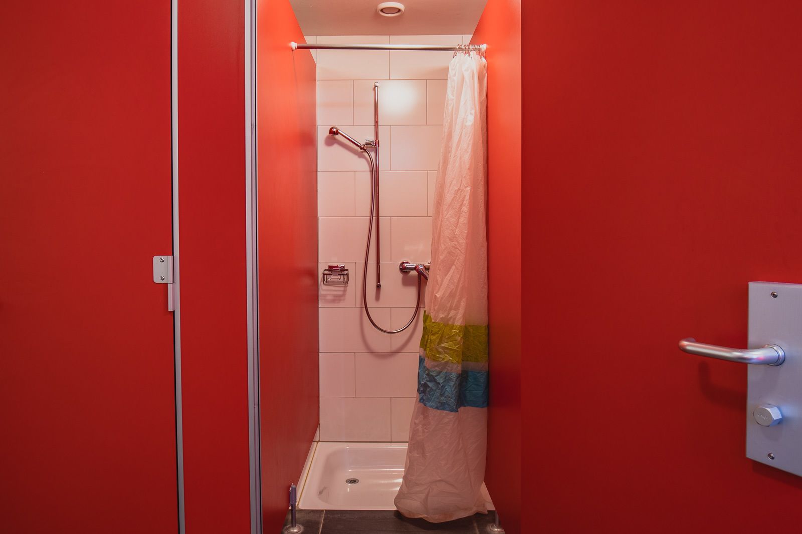 A small, red-walled bathroom with a shower, a towel rack, and a toilet.