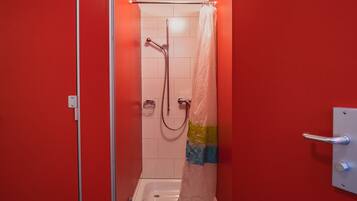 A small, red-walled bathroom with a shower, a towel rack, and a toilet.