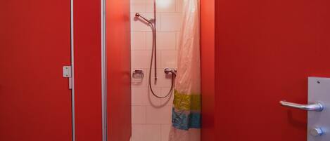 A small, red-walled bathroom with a shower, a towel rack, and a toilet.