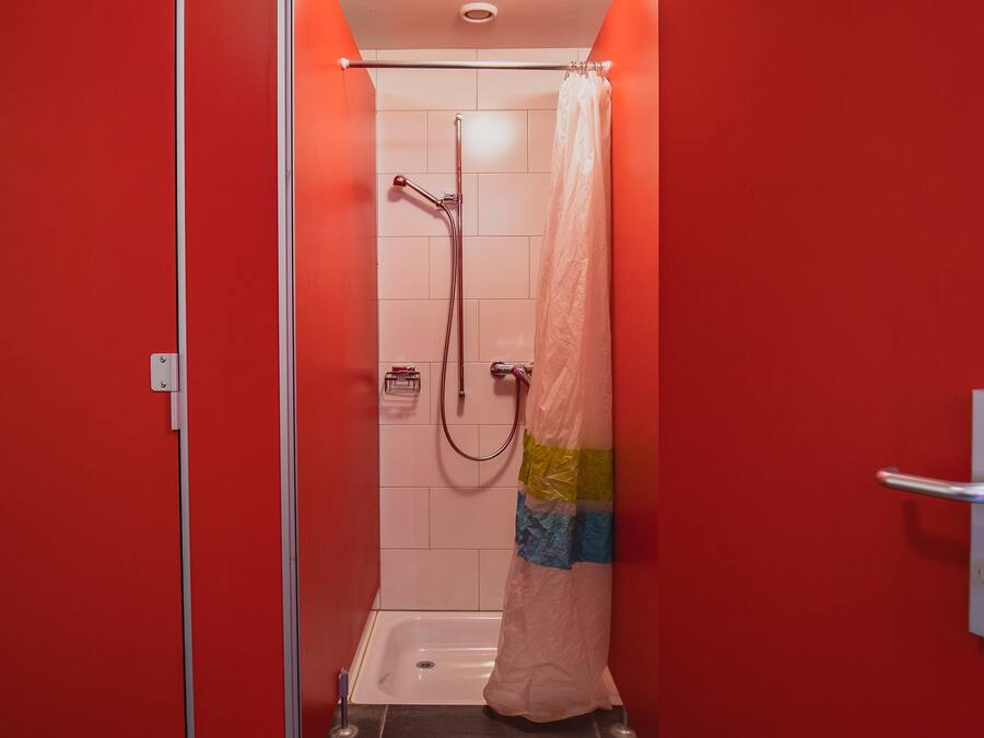 A small, red-walled bathroom with a shower, a towel rack, and a toilet.