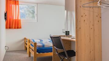 Une petite chambre avec un lit simple, un bureau et une chaise.