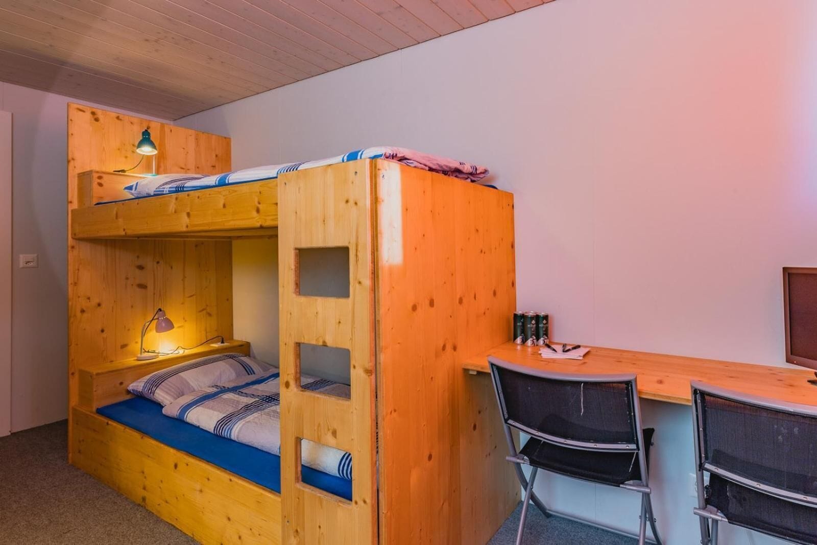 Un lit superposé avec un bureau et des chaises, une lampe et un téléviseur.