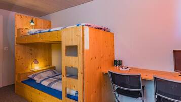 A bunk bed with a desk and chairs, a lamp, and a television.