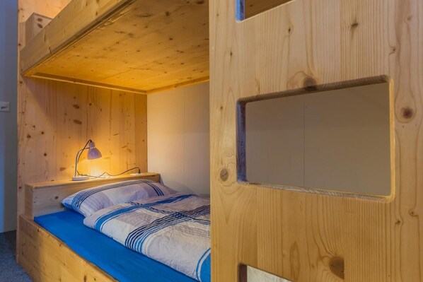 A bunk bed with a desk and lamp, wooden walls, and a window. - Mountain Lodge Backpackercamp (Lenk)