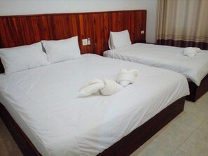 A hotel room with two beds, wooden headboards, white linens, and a towel on the bed.