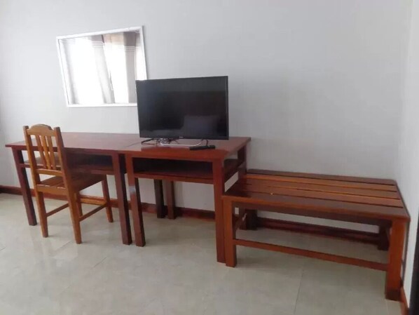 A room with a wooden desk, a television, and a bench. - Phouluang Hotel (Phonsavan)