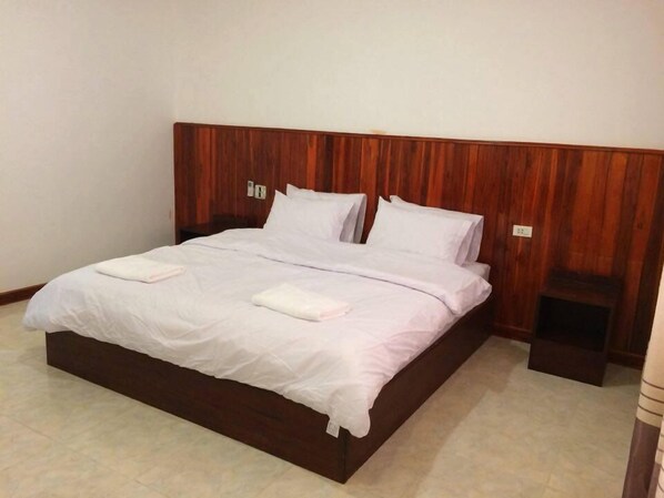 Una cama bien hecha con sábanas y almohadas blancas, un cabecero de madera y una mesita de noche con una lámpara.