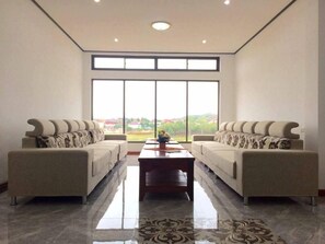 Una sala de estar amplia con dos sofás enfrentados, una mesa de centro en el medio y ventanas grandes que ofrecen vistas al exterior.