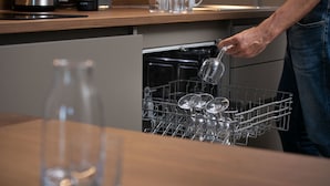 Una persona cargando un lavavajillas con vasos transparentes y una olla de metal.