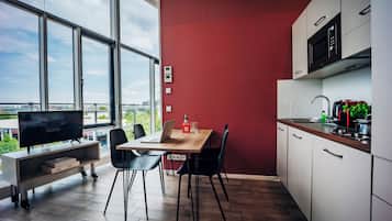 Una cocina moderna con una pared de acento roja, un área de comedor con mesa y sillas, un televisor y vistas de la ciudad a través de amplias ventanas.