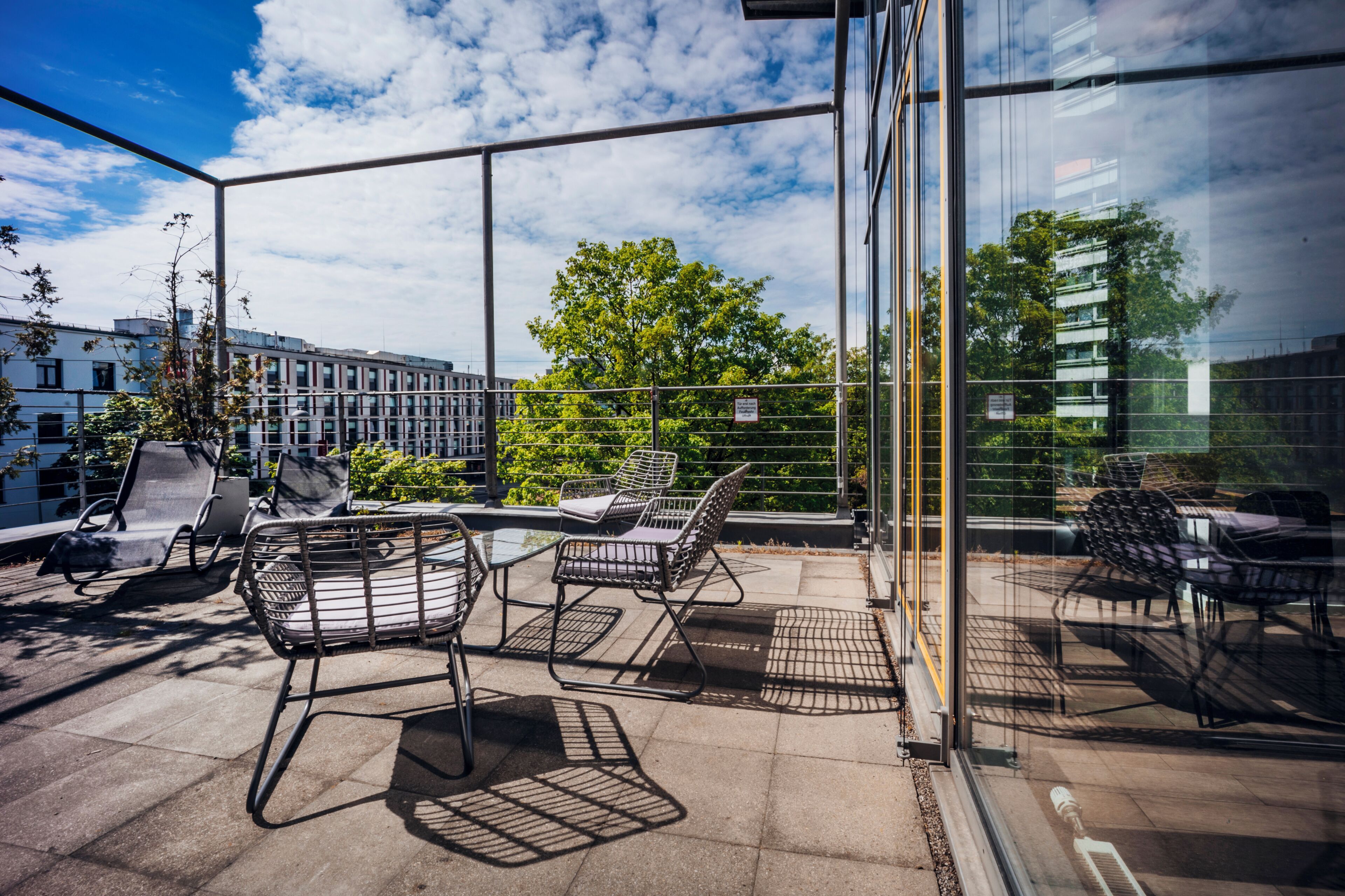 Una terraza en la azotea con mobiliario exterior y una barandilla de cristal.