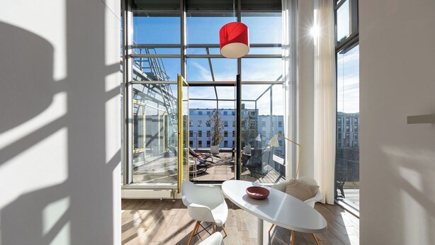 Una habitación moderna con un ventanal grande, una mesa blanca y una lámpara colgante roja.