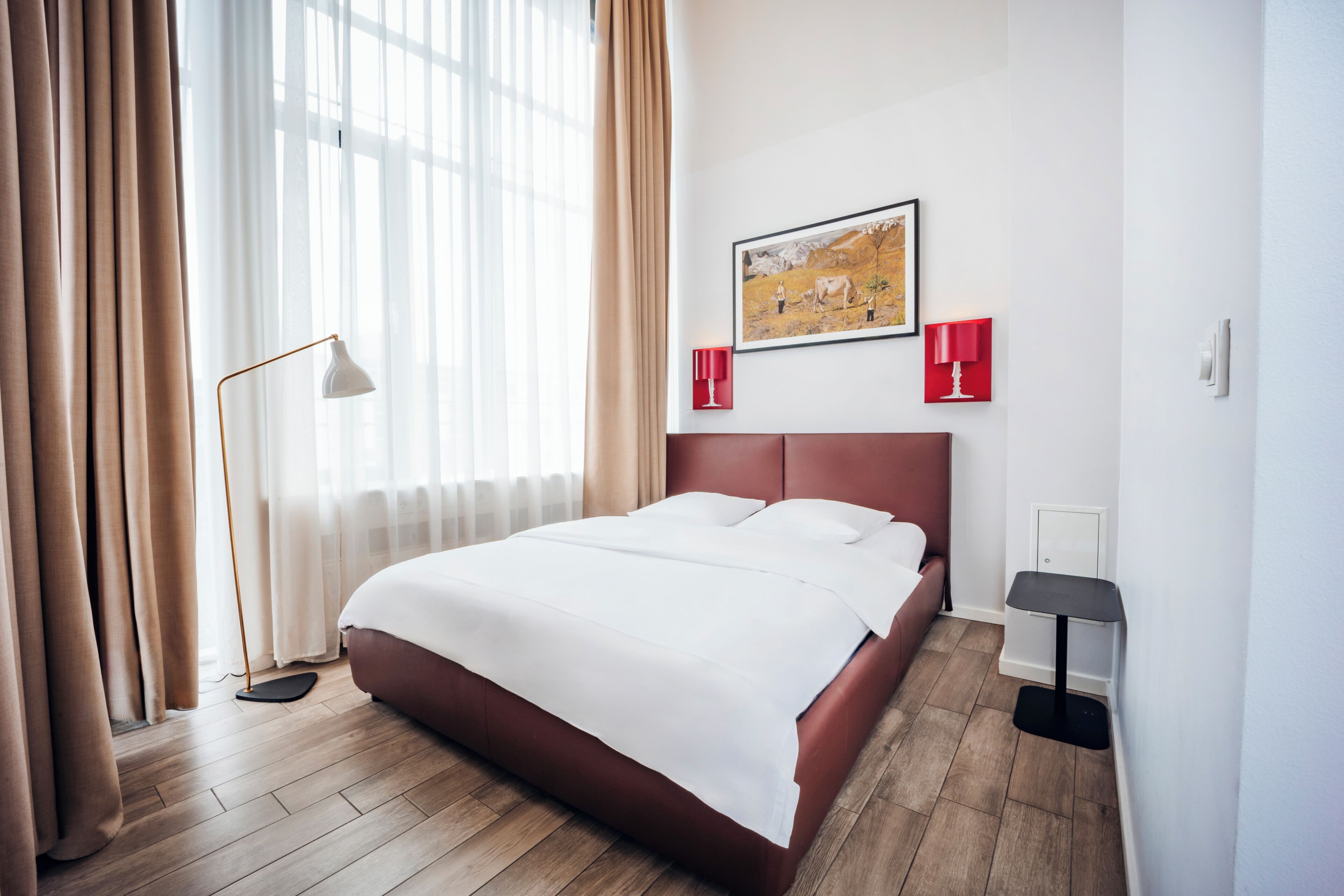 A hotel room with a bed, a painting, a floor lamp, and a bedside table.