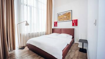 A hotel room with a bed, a painting, a floor lamp, and a bedside table.