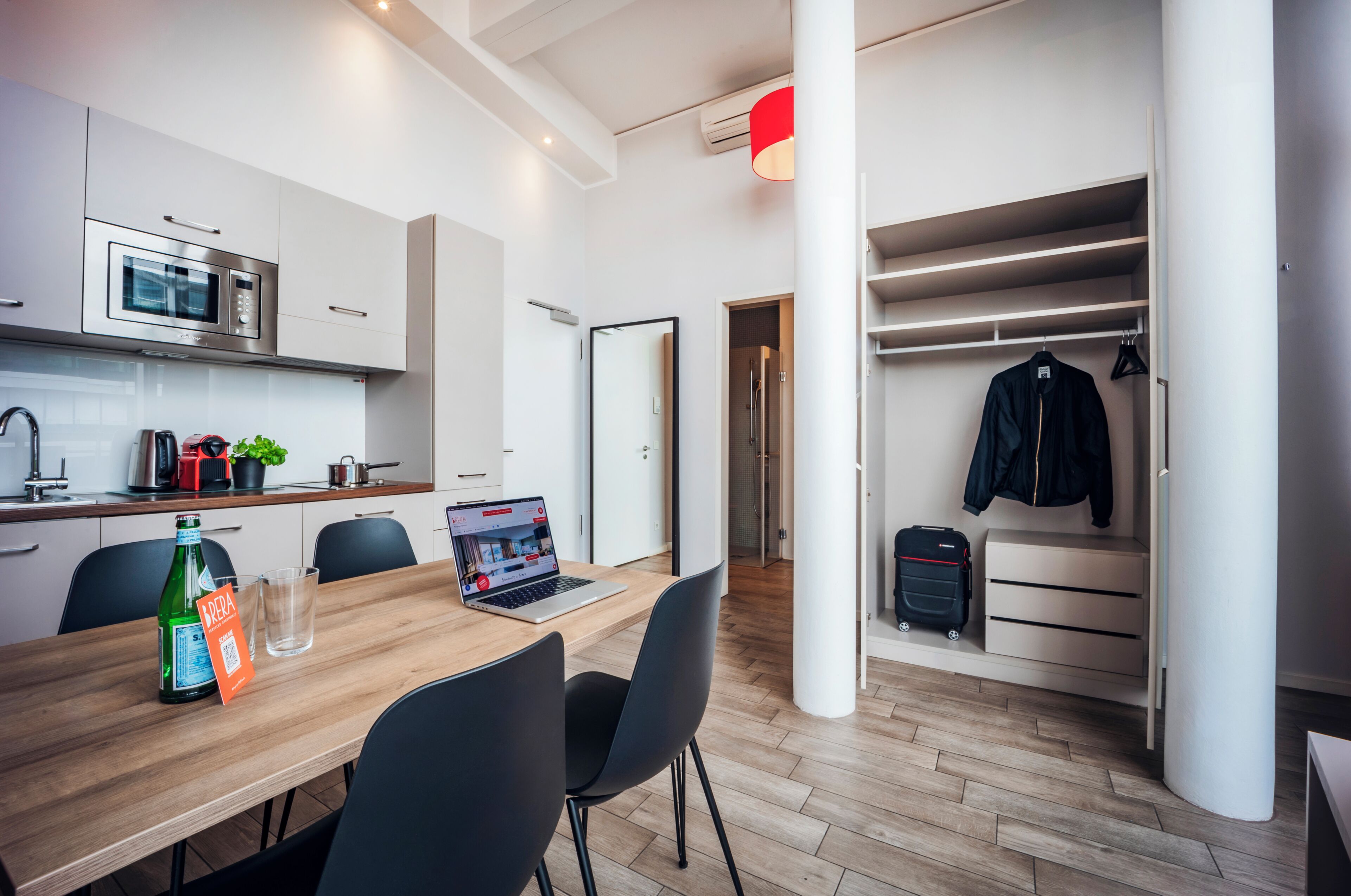 Eine moderne Küche mit Mikrowelle, Toaster und Kaffeemaschine, ein Essbereich mit einem Laptop und ein begehbarer Kleiderschrank mit Kleidung.