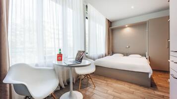 A hotel room with a bed, a desk with a laptop, a chair, and a bottle of water.