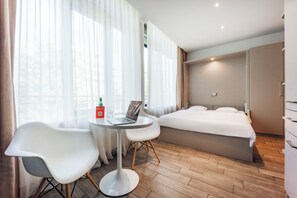 A hotel room with a bed, a desk with a laptop, a chair, and a bottle of water. - Brera Serviced Apartments Munich West (Munich)