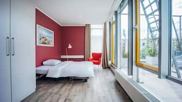Habitación de hotel moderna con una cama, un escritorio, una silla y ventanas amplias con vistas al exterior.