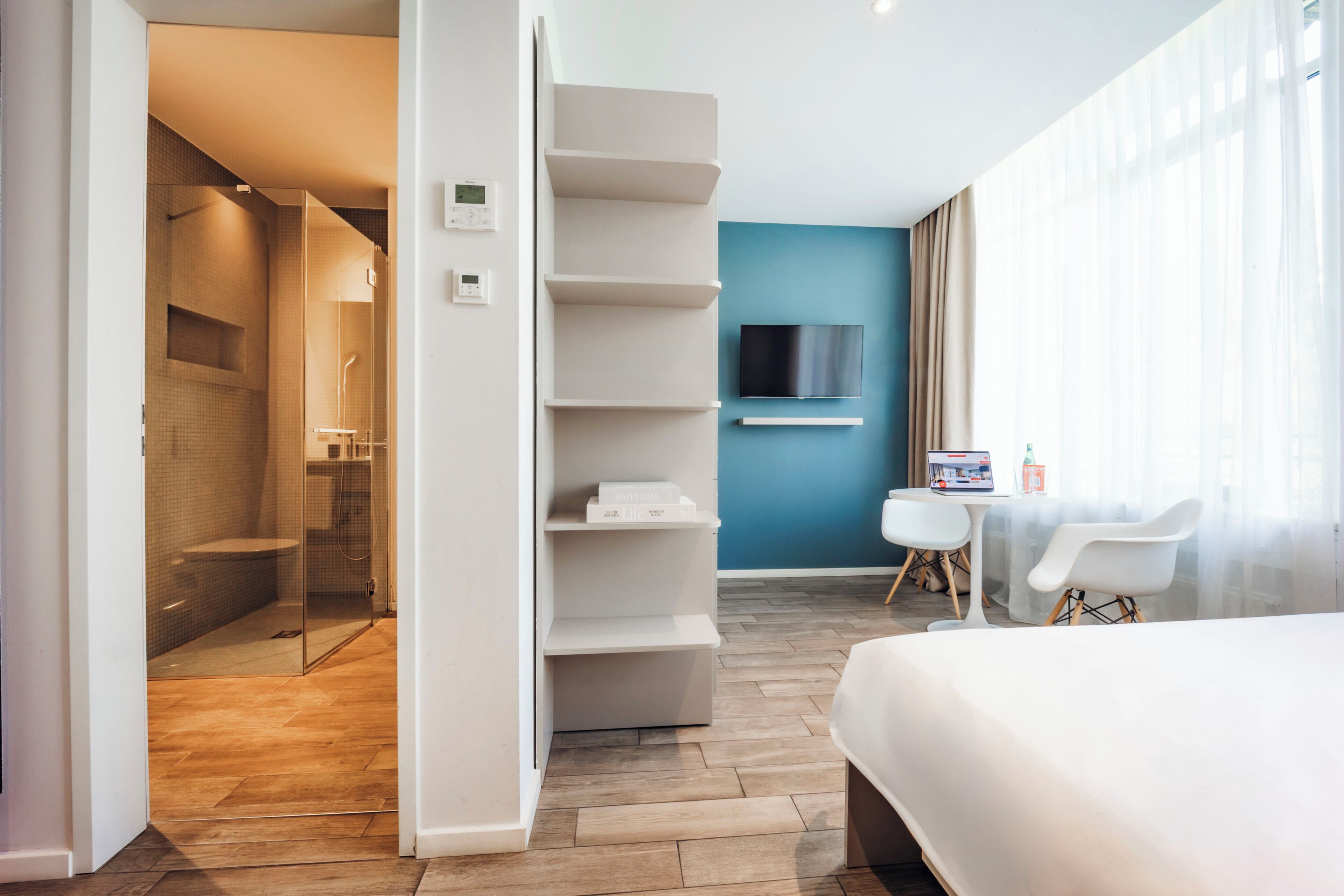 Een moderne hotelkamer met douche, bed, televisie en een klein tafeltje met stoelen.
