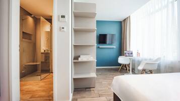 Una habitación de hotel moderna con ducha, cama, televisor y una pequeña mesa con sillas.