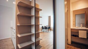 A modern interior with a built-in shelving unit, a dining area with chairs, and a bathroom with a mirror and sink.