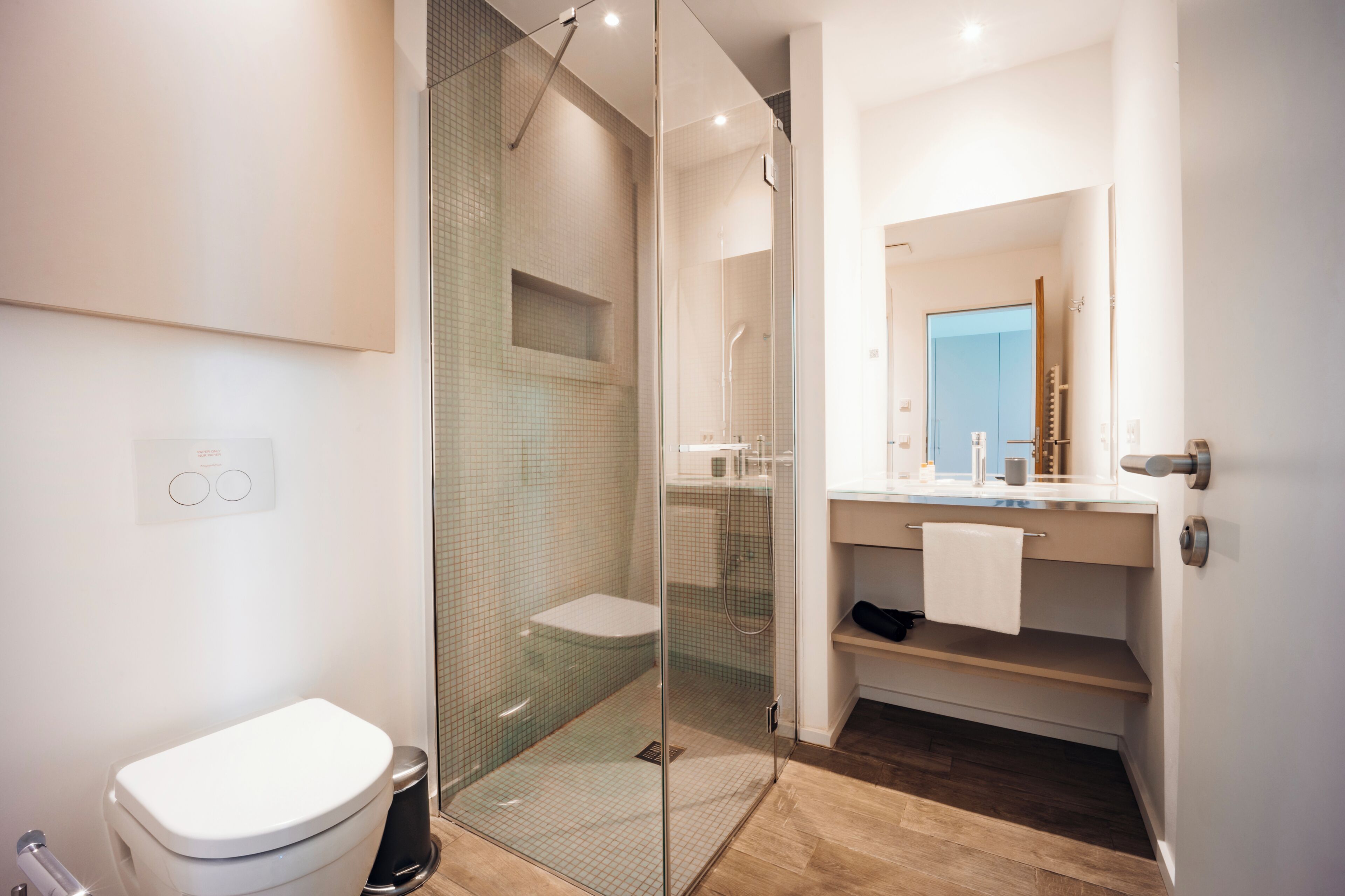 A modern bathroom with a glass-enclosed shower, a white toilet, and a vanity with a mirror.