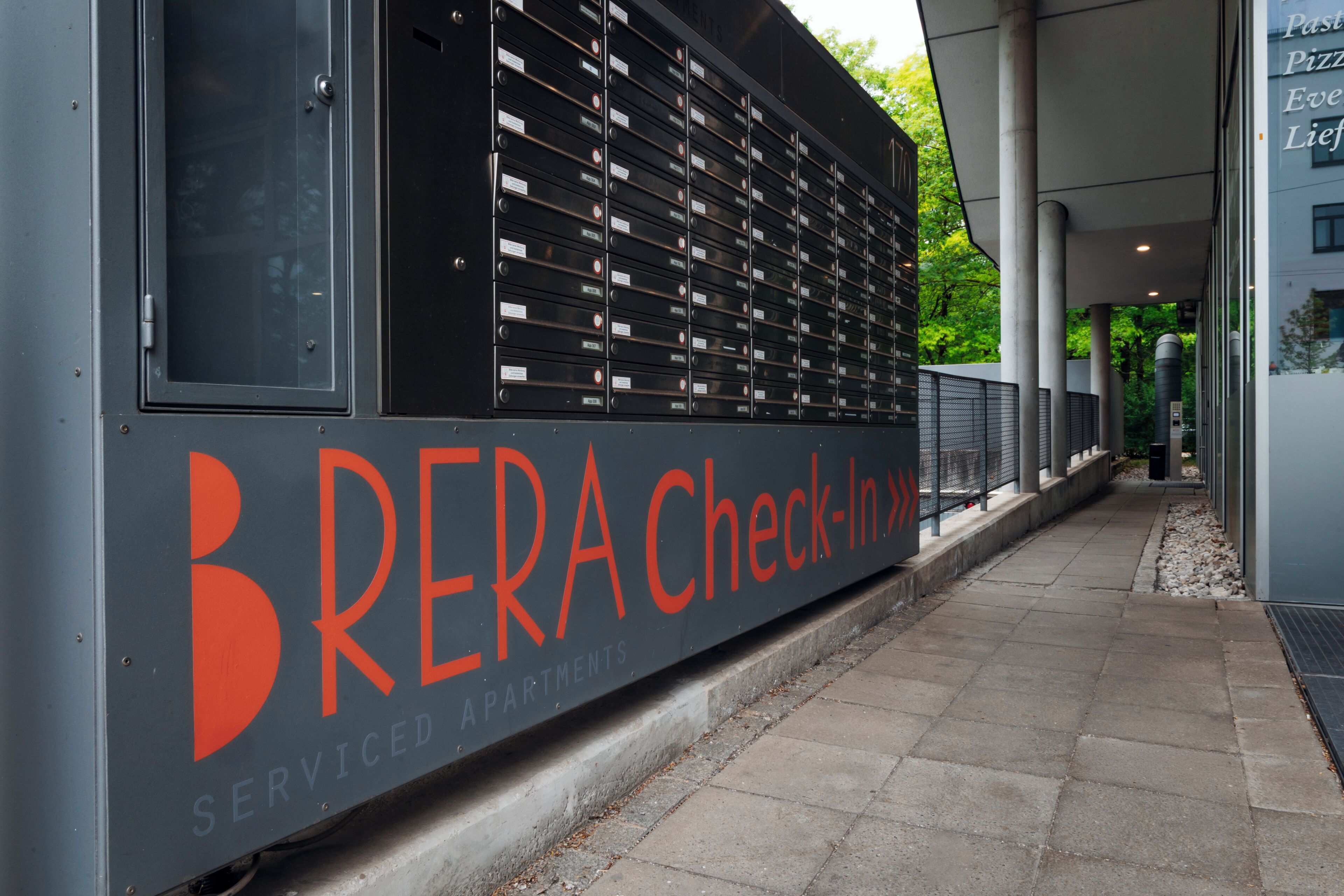 A building facade with a row of mailboxes and a sign that reads 'BRERA Check-In >'.
