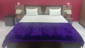 A bed with a purple blanket, two white pillows, and two bedside tables with lamps. - Hotek Aarti Inn (Ballia)
