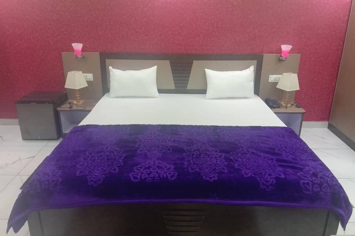 Ein Bett mit einer violetten Decke, zwei weißen Kissen und zwei Nachttische mit Lampen.