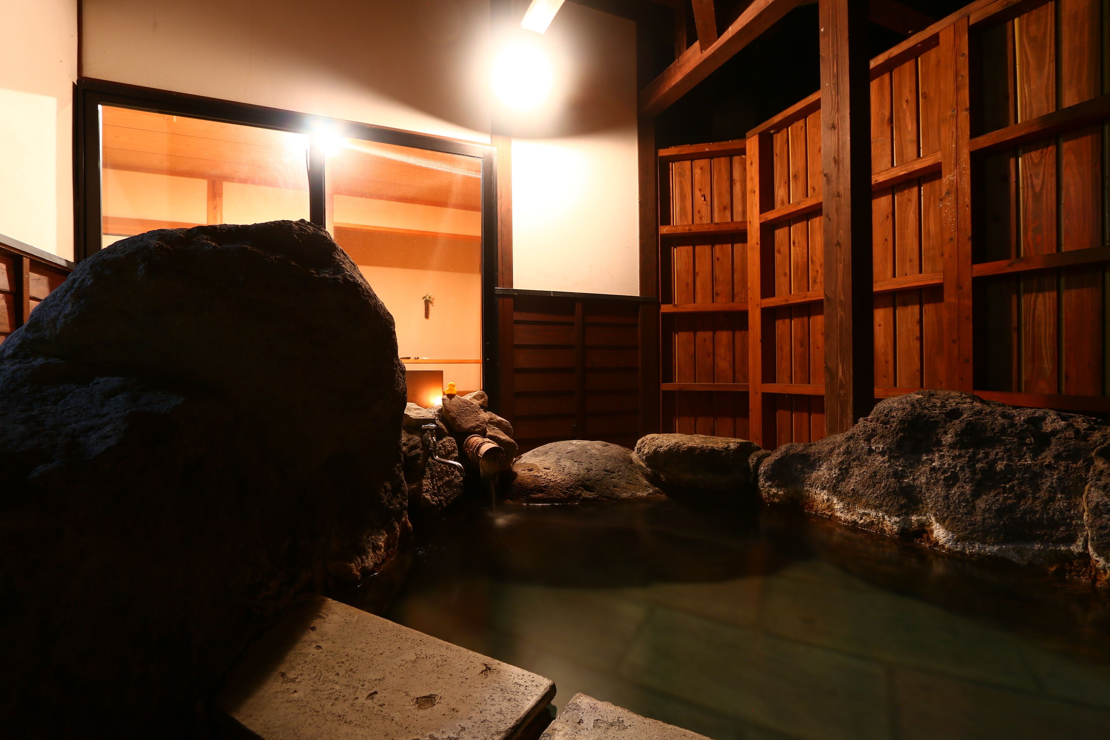 Un onsen japonais traditionnel, avec une architecture en bois, un bain en pierre et une petite cascade.